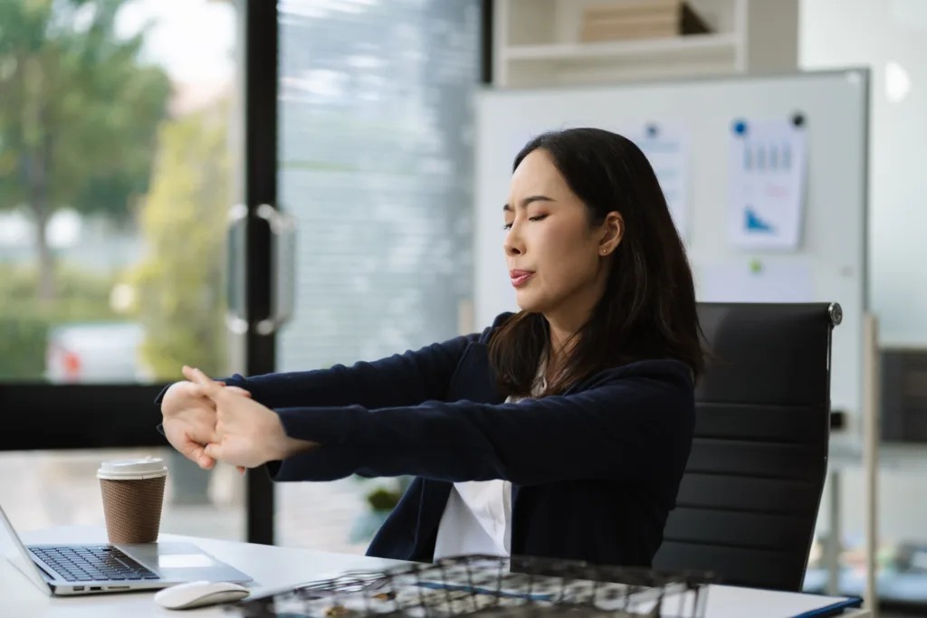 Office worker stretching at desk during movement break in modern London office.
